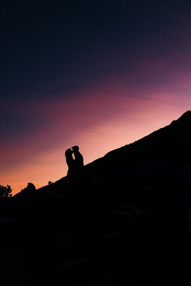 Vacation Photographer, silhouette of man and woman kiss before setting sun while standing on mountain grade