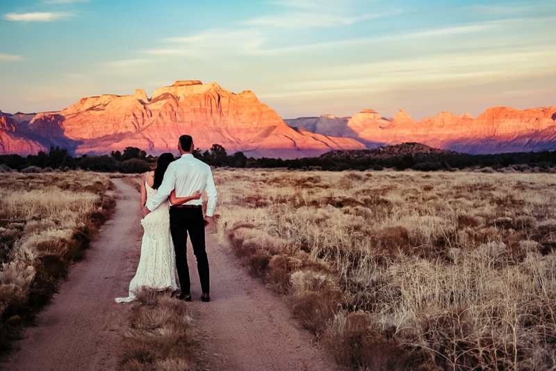 Elopement Photographer, a bride and groom walk down a path through dry shrubs in the wilderness