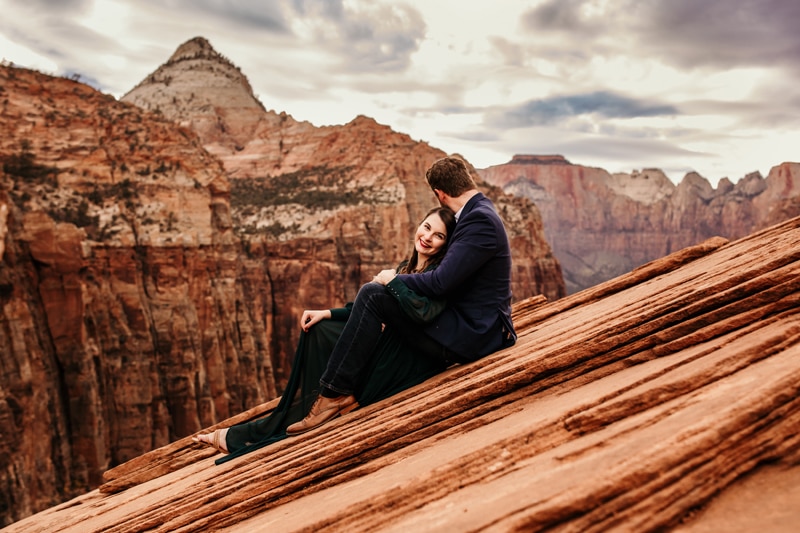 Vacation Photographer, a man and woman sit together smiling as they sit atop Zion's high canyon walls