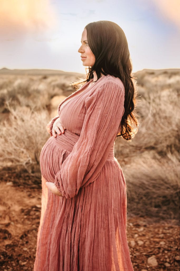 Maternity Photographer, an expectant mother holds her pregnant belly outside