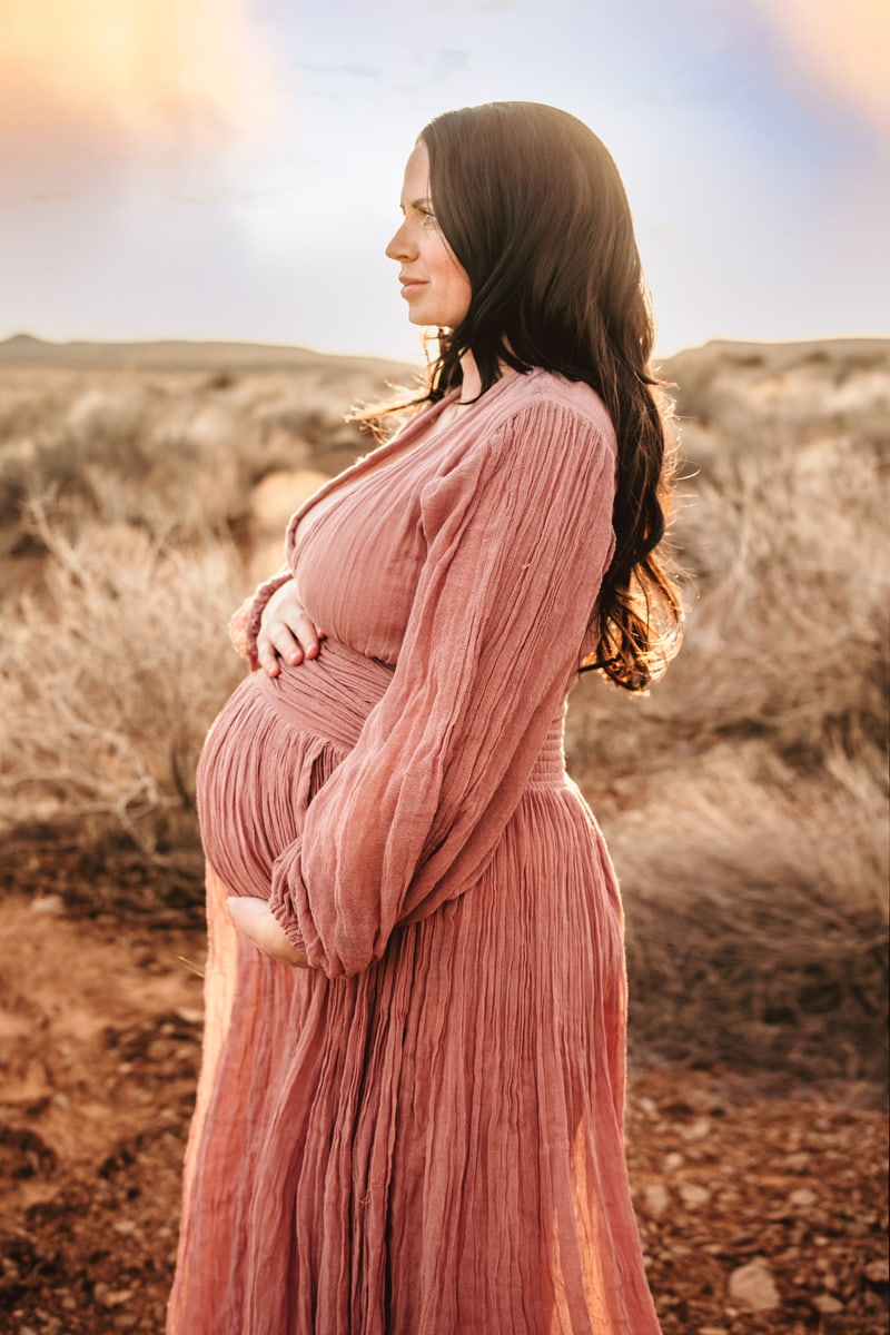 Motherhood Photographer, a pregnant woman holds her belly outdoors, she is anticipating baby