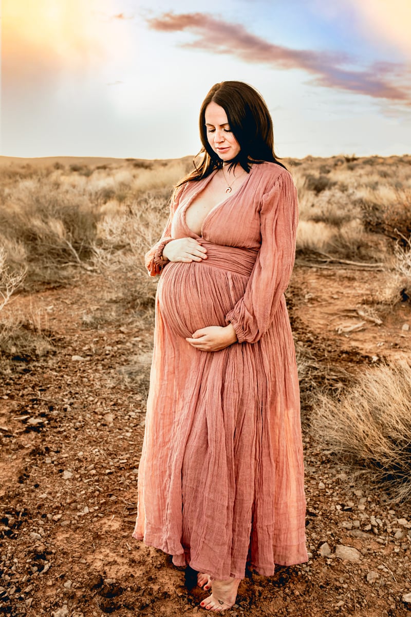 Motherhood Photographer, pregnant woman wears long dress and holds her belly happy in expectation of baby