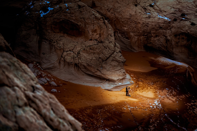 Vacation Photographer, a man and woman draw close in the sands beneath the tall canyon walls in Zion