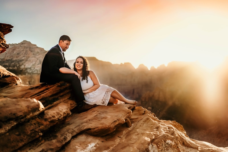 Elopement Photographer, a bride in her dress leans on the lap of her groom, the sit on a sandstone wall outdoors