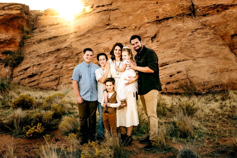 Vacation Photographer, Family of six stand before rock wall, standing in shrubs, brother and sisters draw close.
