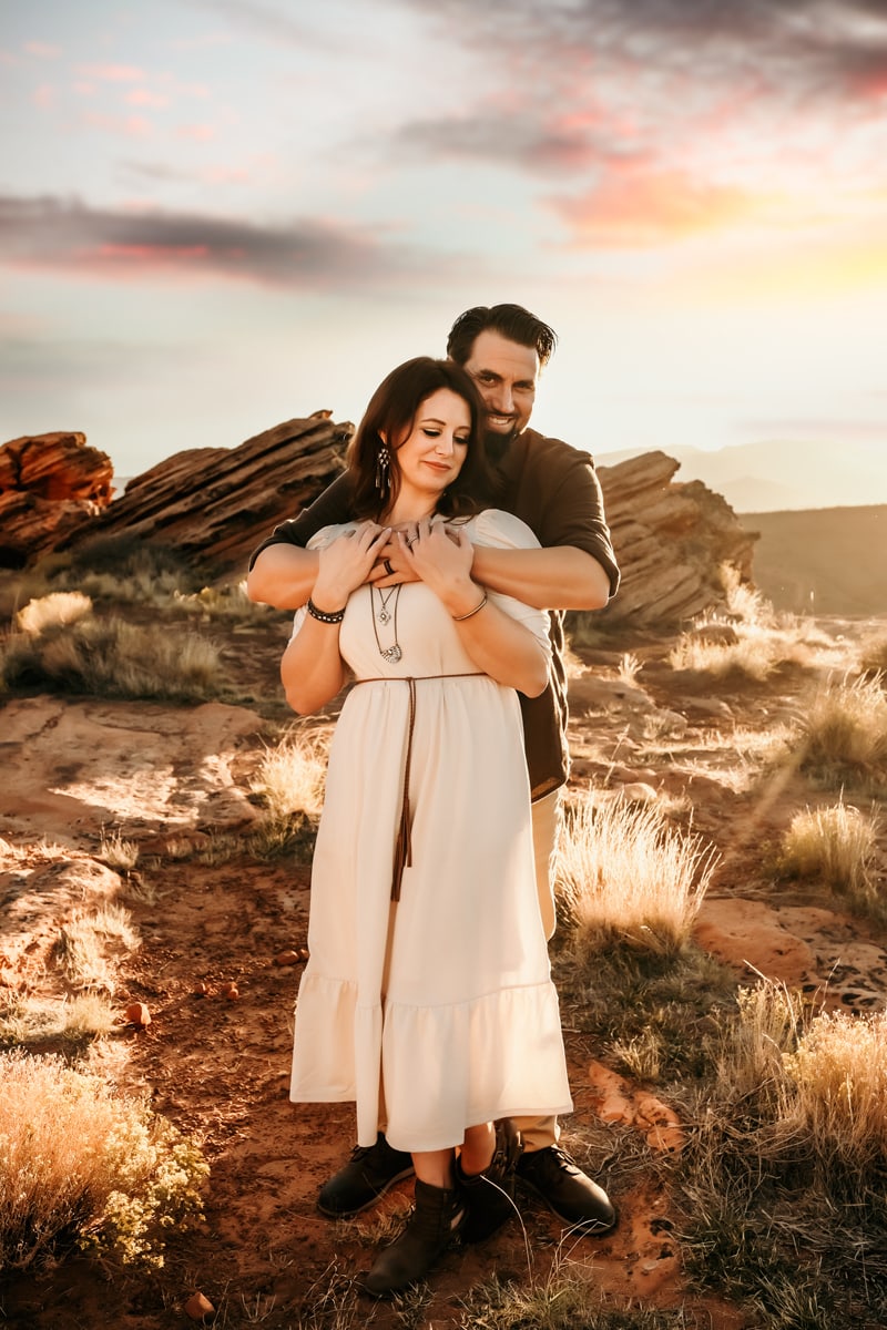 Vacation Photographer, a man embraces his wife from behind in the Utah desert, they both are happy
