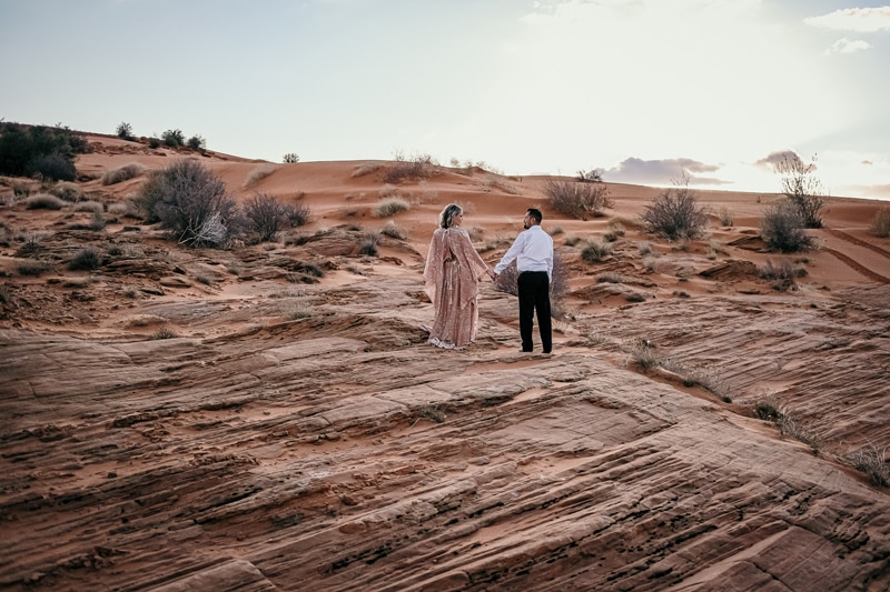 Elopement Photographer, newly married husband and wife walk hand in hand on desert rock
