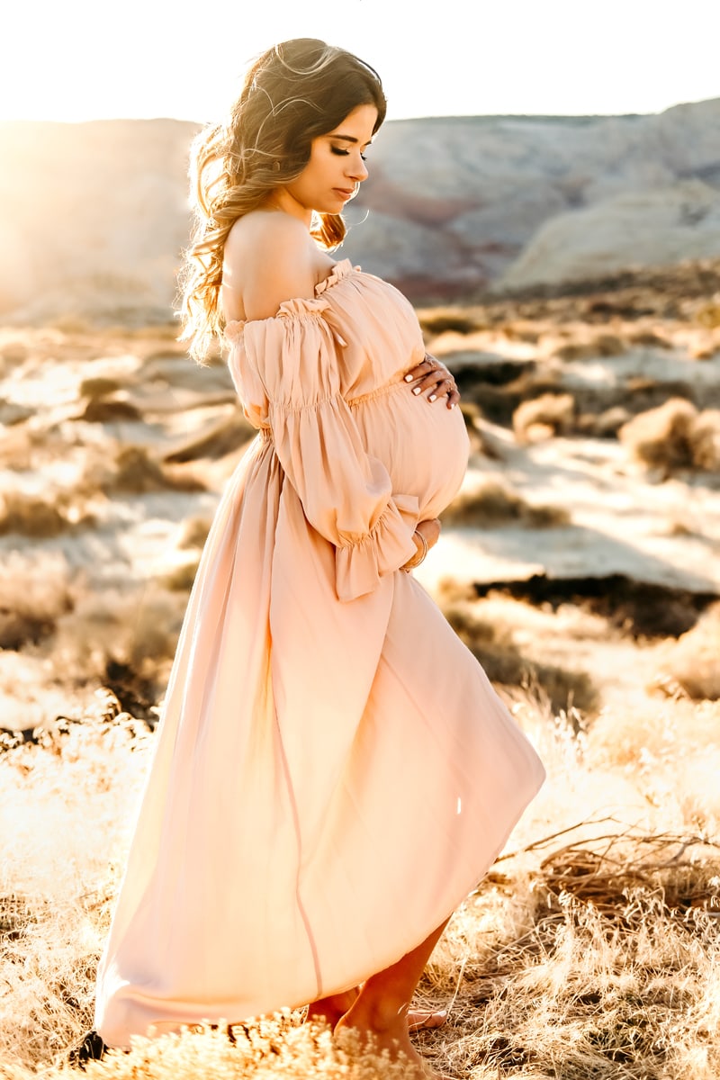 Motherhood Photographer, a pregnant woman stands in the desert with her hands on her belly