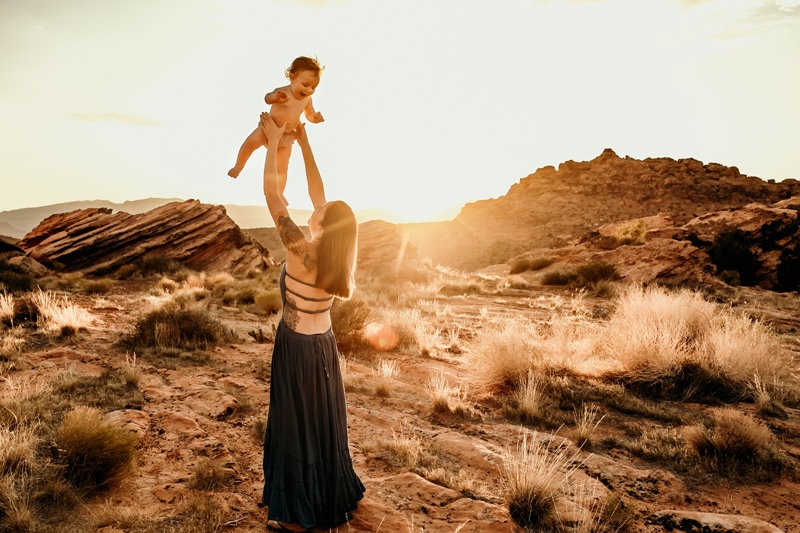 Motherhood Photographer, a mother throws her happy young baby in the air, they are in the desert