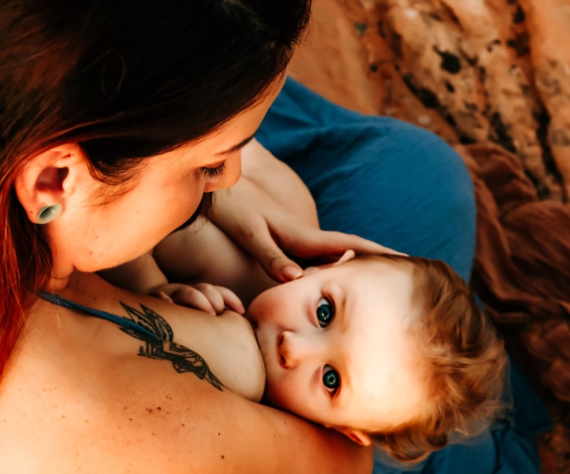 Motherhood Photographer, a mom breastfeeds her young child, she looks at him fondly