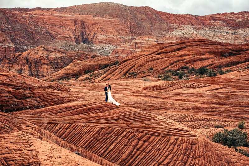 Elopement Photographer, a bride and groom stand atop red rock hills in the distance