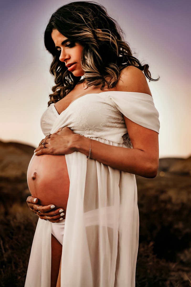 Motherhood Photographer, a pregnant woman holds her belly at dusk