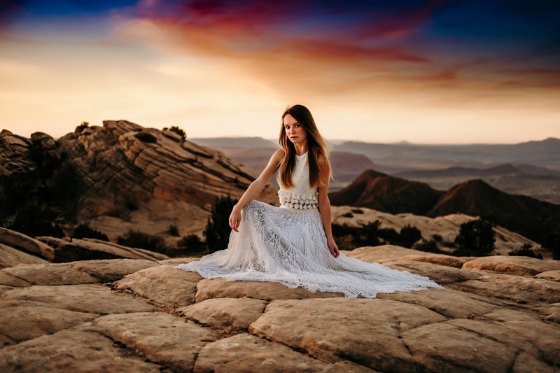 Elopement Photographer, a bride kneels on Utah's sandstone before the desert at sunset