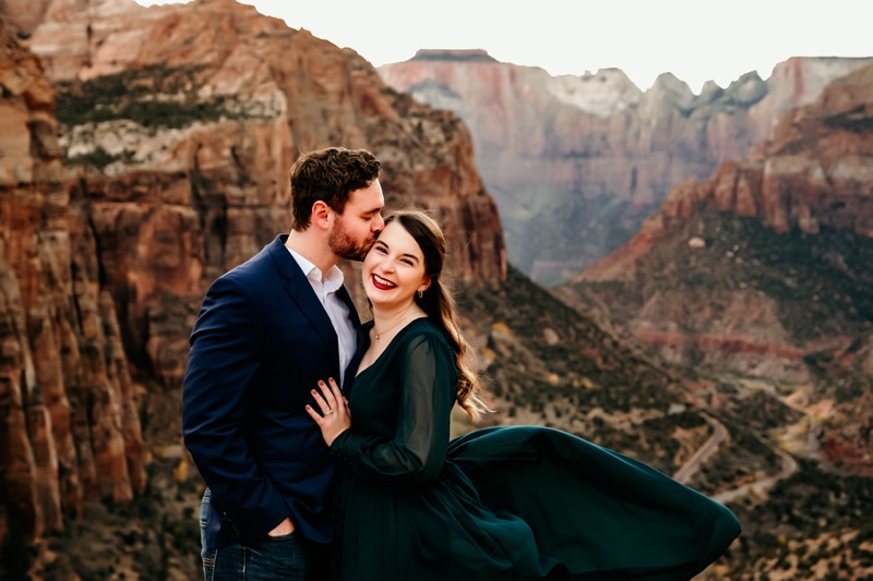 Vacation Photographer, a husband kisses his wife on the forehead, she smiles, they are in Zion