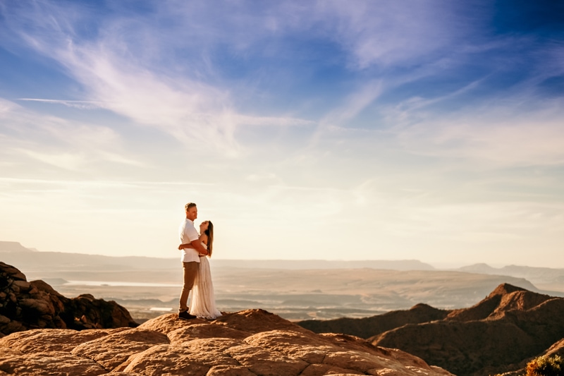 Elopement Photographer, atop a mountain scape, a.couple hold each other with Utah wilderness in the vast distance