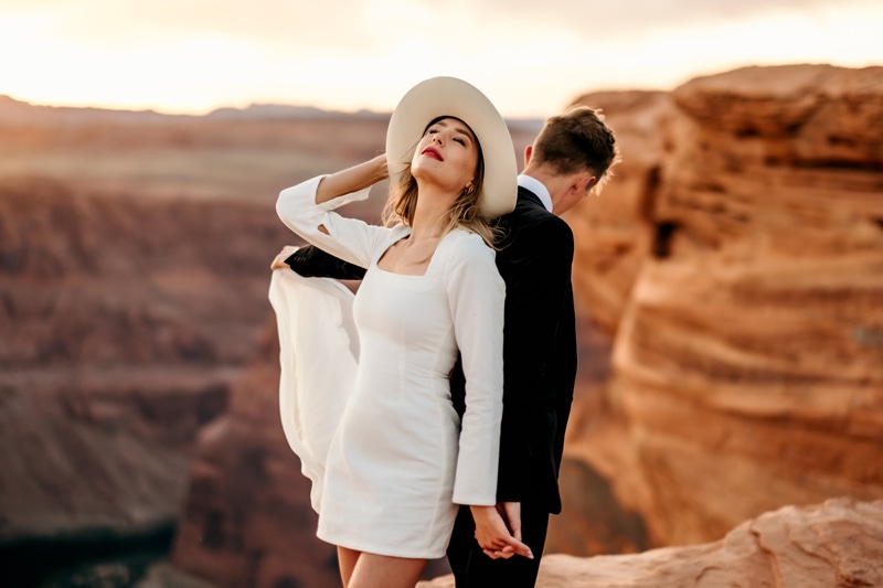 Elopement Photographer, a young bride and groom hold hands, back to back before Utah's Canyons