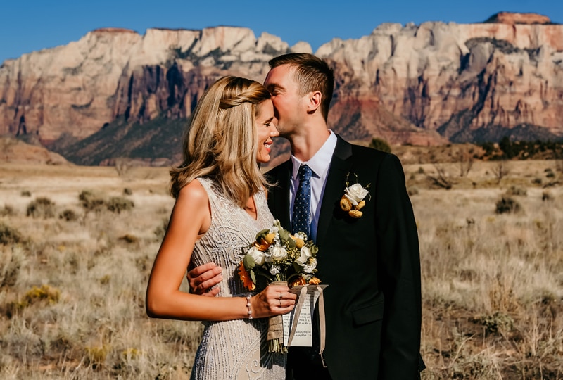 Elopement Photographer, a groom kisses his new bride on the head in a desert wilderness outdoors
