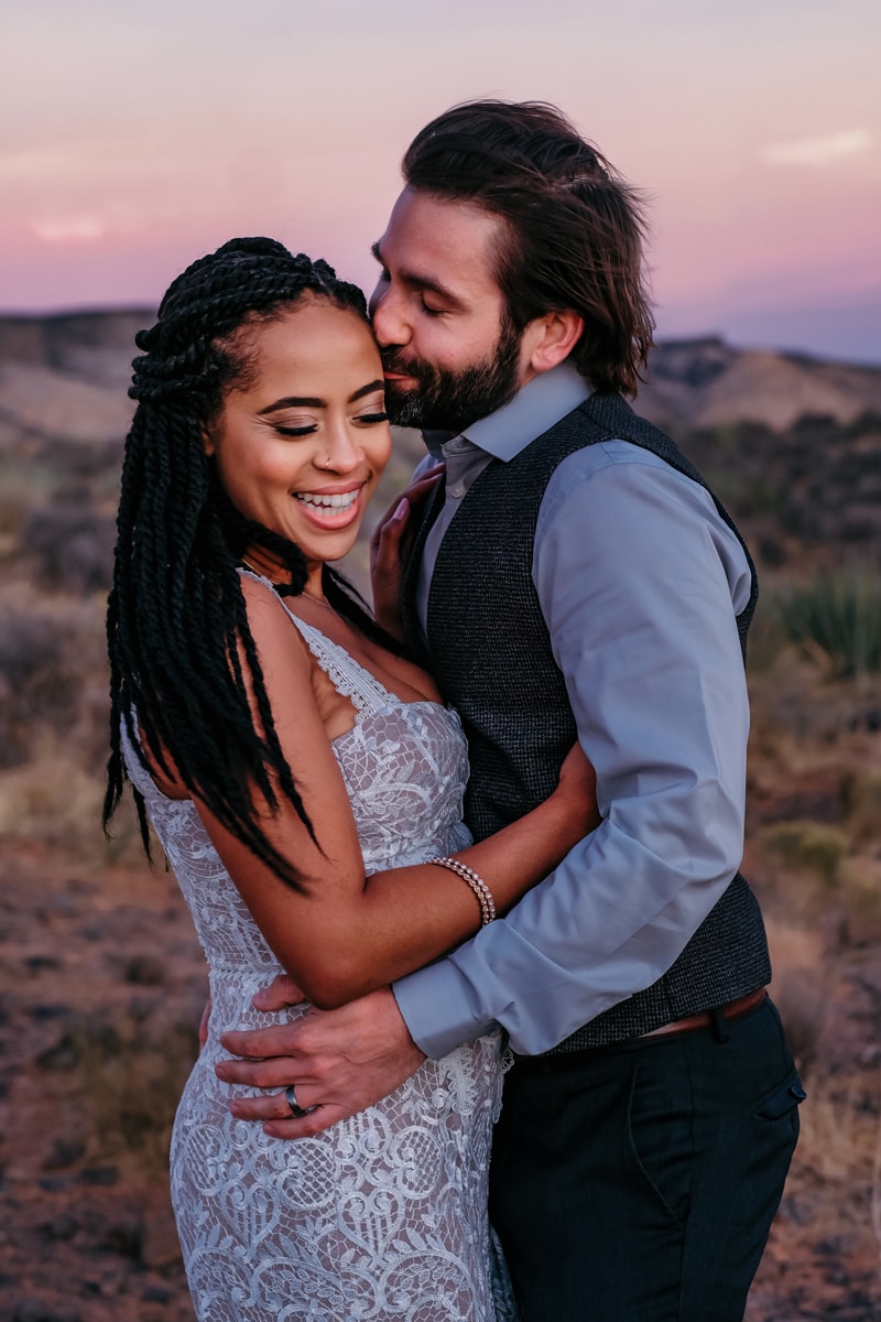 Elopement Photographer, a young couple hold each other closer, he kisses her at sunset