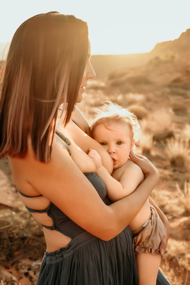 Motherhood Photographer, mother stands in the desert while breastfeeding young baby
